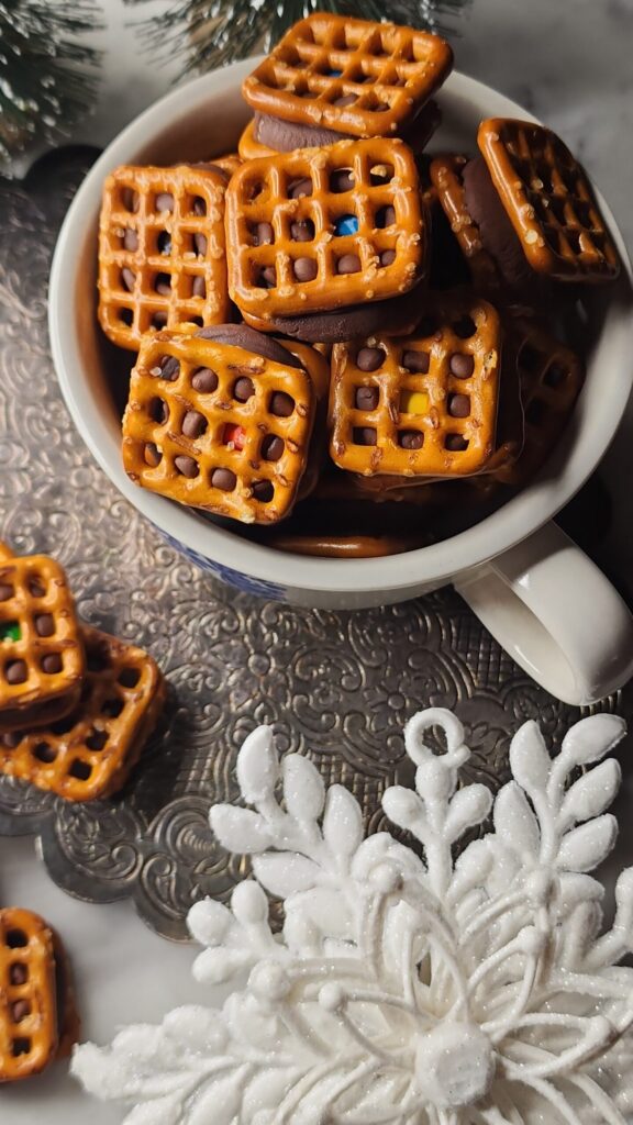 A mug full of sweet and salty Christmas candy on a silver trivet with festive holiday accents.