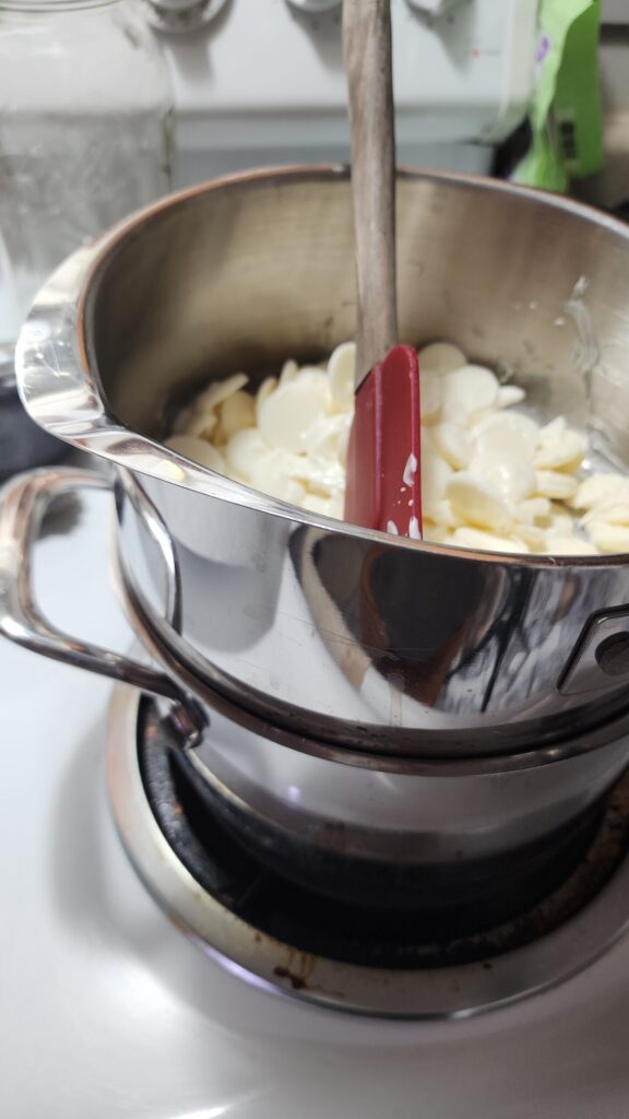 Two pans are stacked creating a double boiler to melt white chocolate for Peppermint Bark.