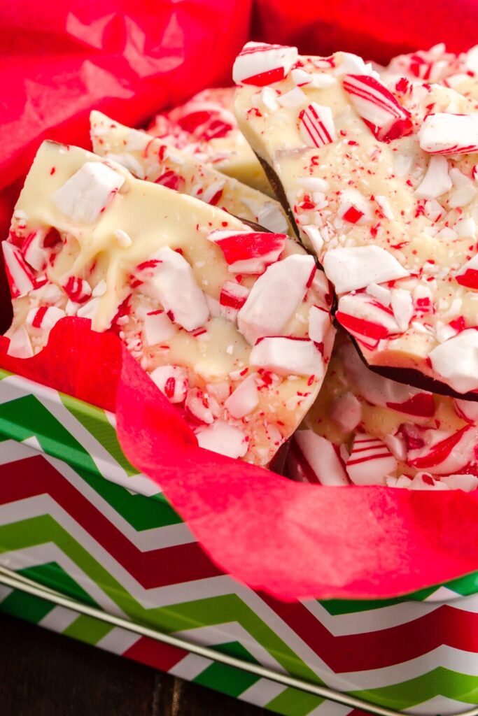 Pieces of peppermint bark lay in a festive holiday tin with red tissue paper.