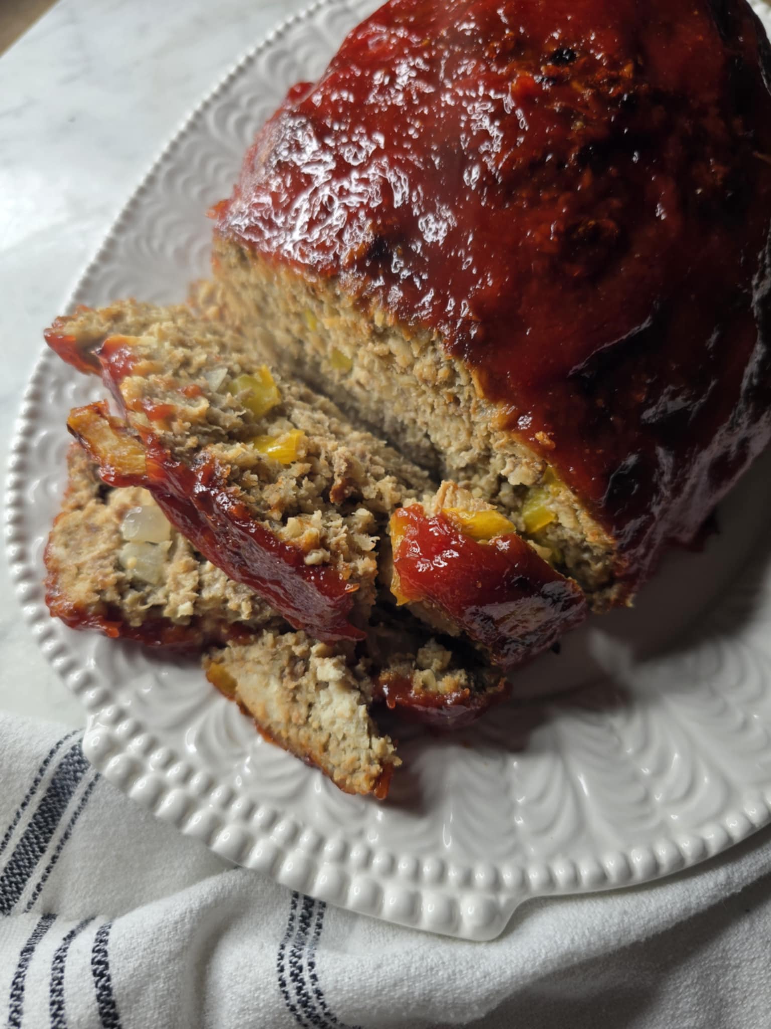 Easy moist meatloaf on a white platter with a striped towel ready to enjoy as a cozy evening family dinner.
