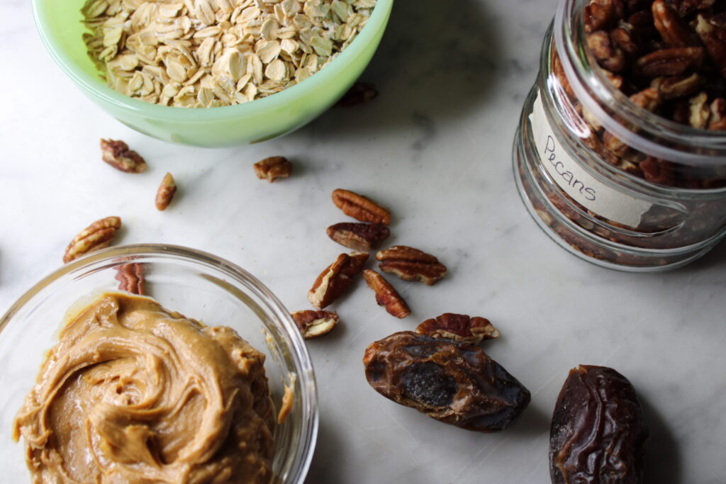 Ingredients for healthy pecan date bars on a marble surface.