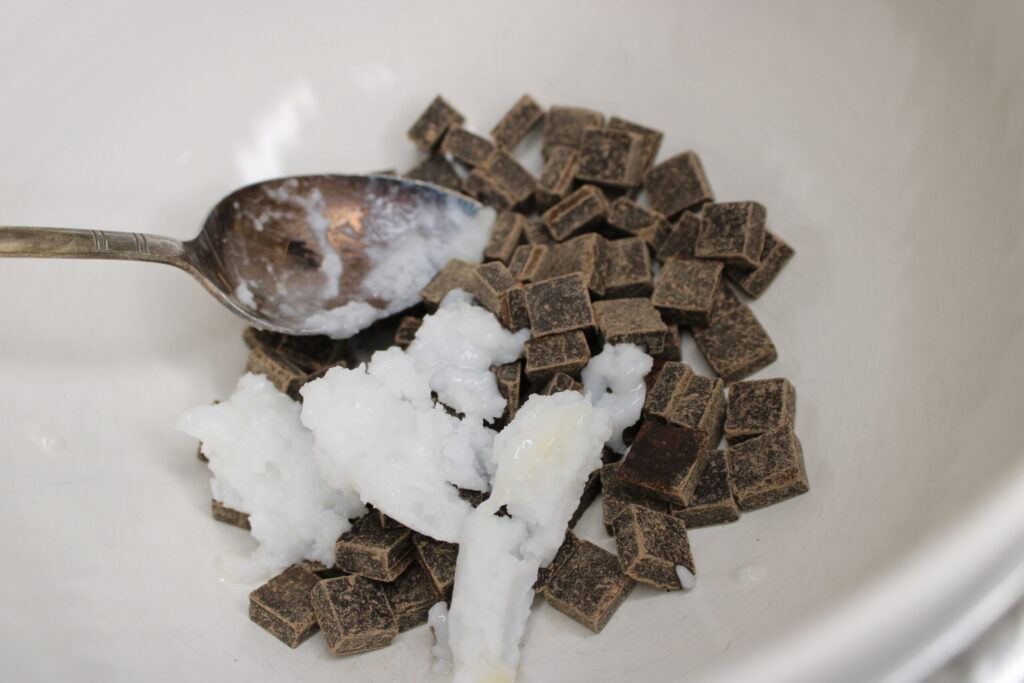 Dark chocolate and coconut oil is being melted in a glass bowl on the stove.