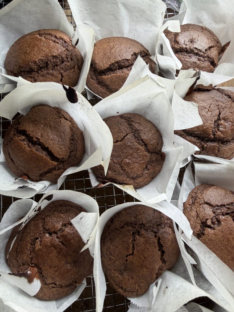 Fresh out of the oven sourdough double chocolate muffins in parchment liners on a cooling rack.