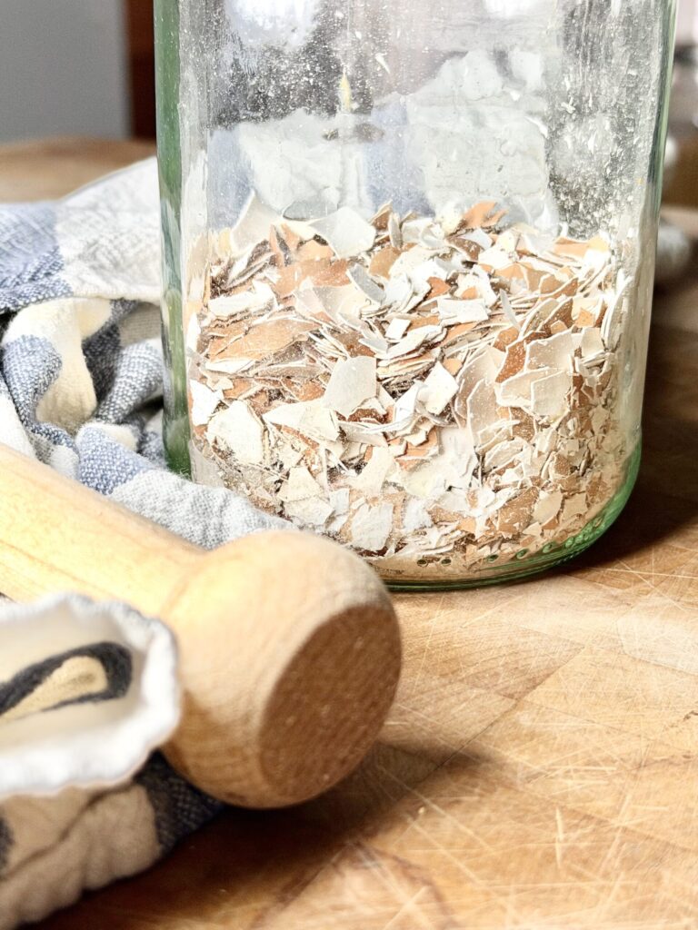 Crushed egg shells in a glass jar on a wooden surface.