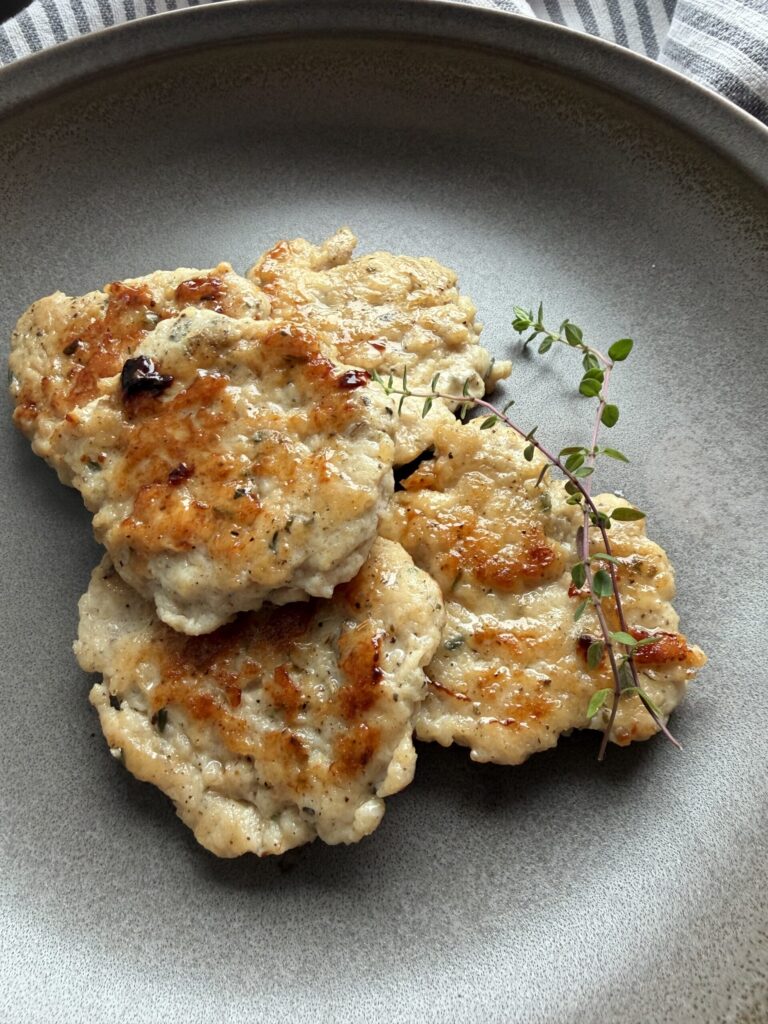 Chicken sausage patties on a plate with fresh thyme sprigs.