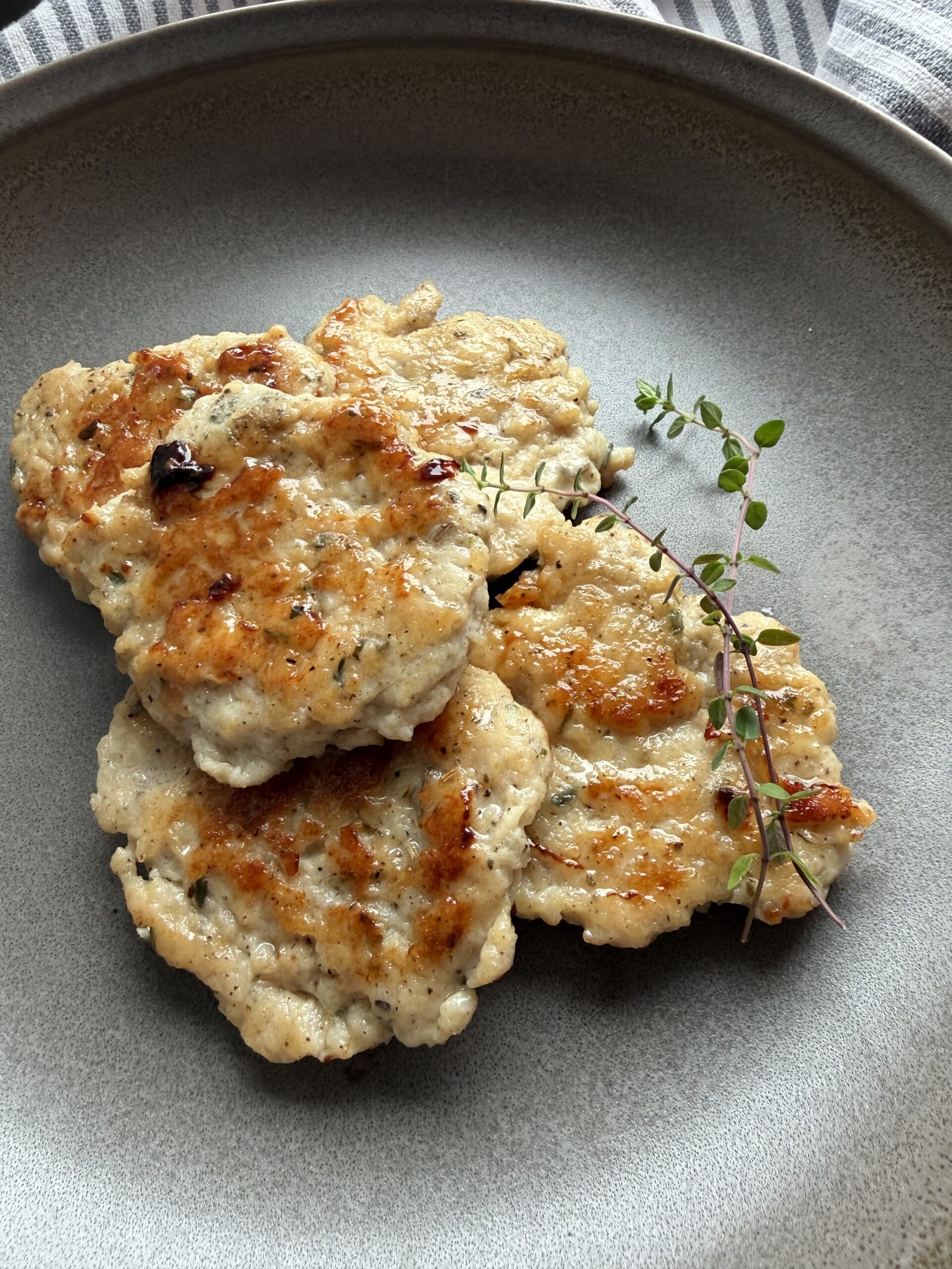 Chicken sausage patties on a plate with fresh thyme sprigs.