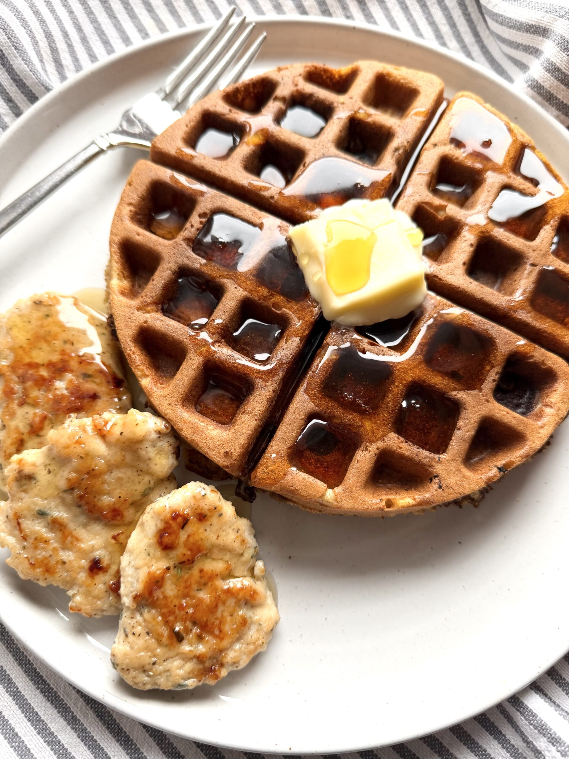 Homemade Chicken breakfast sausage on a plate with a sourdough discard waffle with butter and drizzled with pure maple syrup.