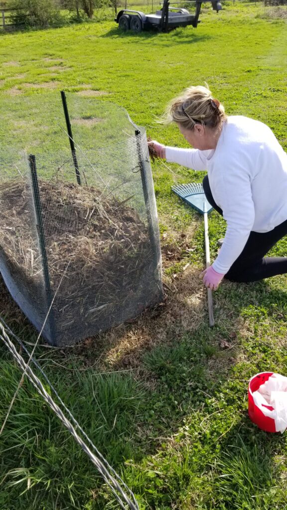 A woman sitting next to her homemade compost bin. 