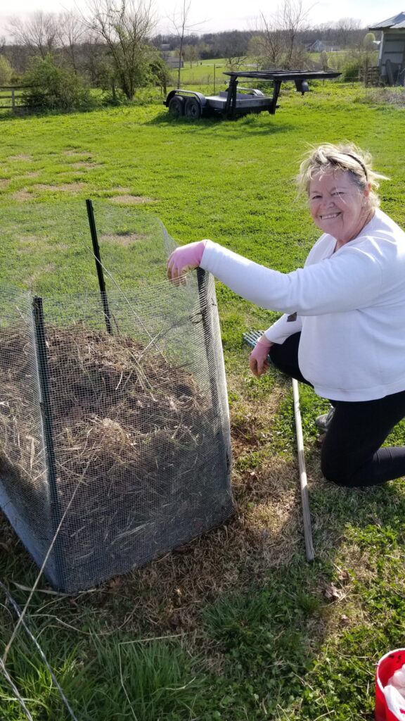A woman in smiling next to her homemade compost bin. 