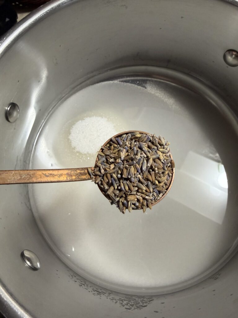 A scoop of fresh lavender petals in being added to sugar water to make a lavender simple syrup. 