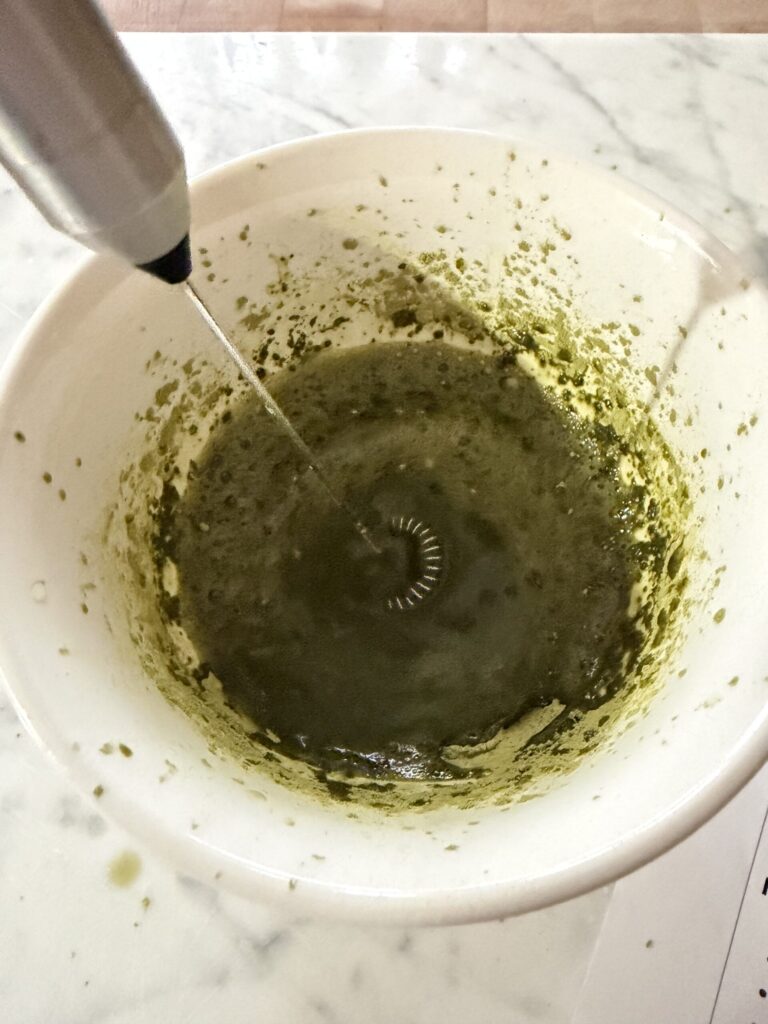 A milk frother mixing matcha tea powder and water to create a matcha tea latte.