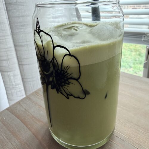 Homemade matcha latte in a glass on a wooden surface.