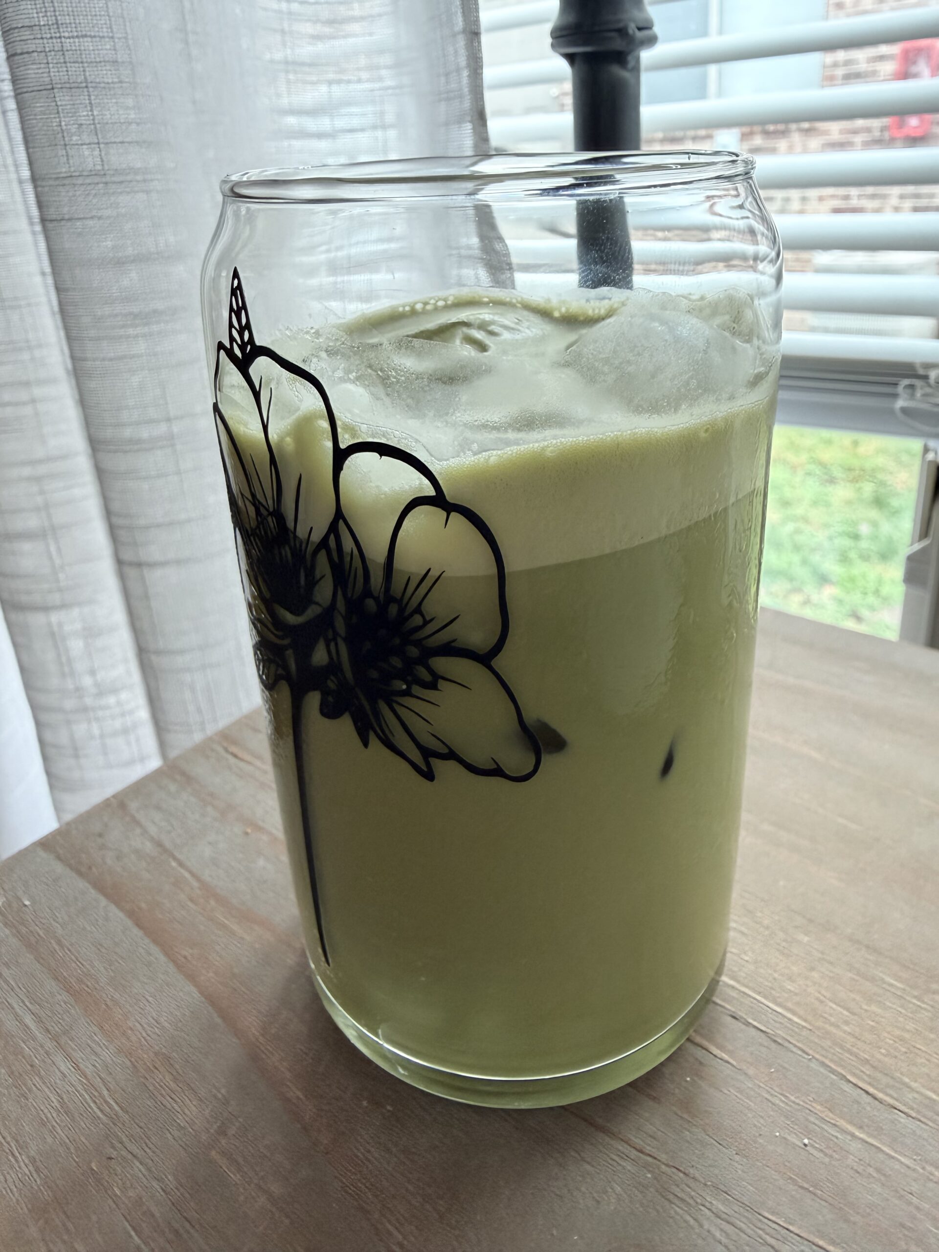 Homemade matcha latte in a glass on a wooden surface.