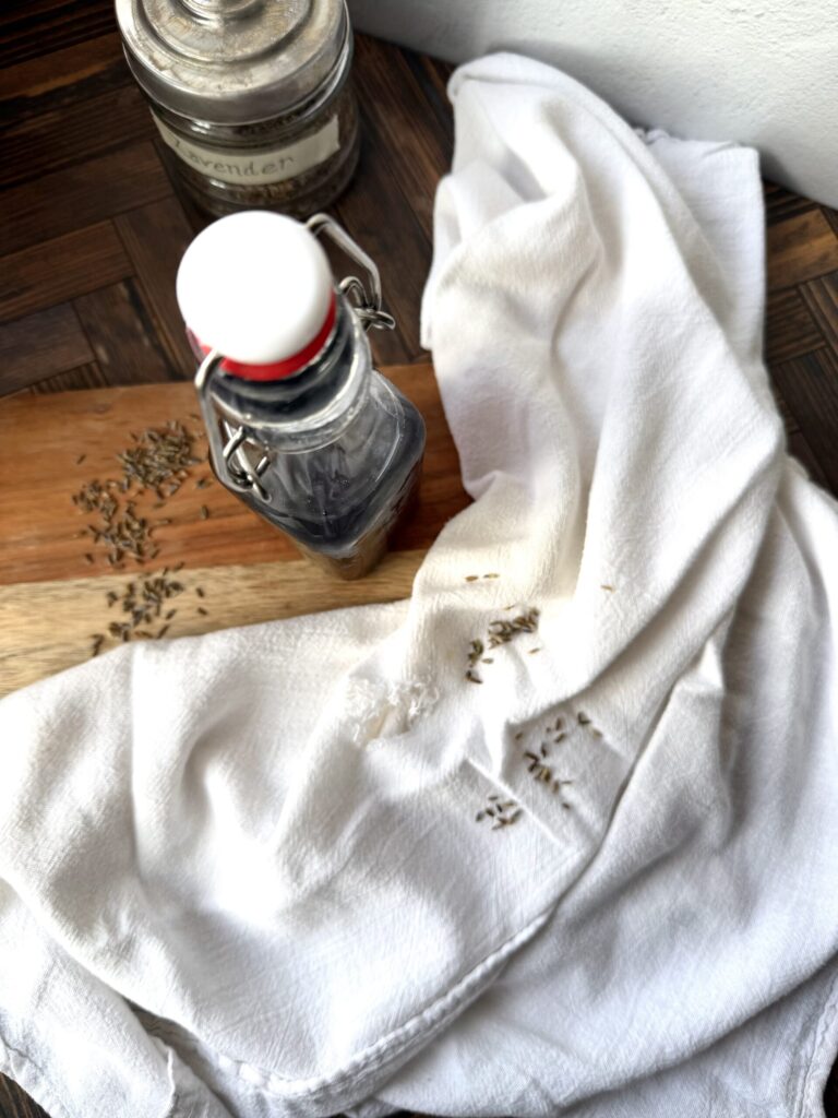 Lavender simple syrup on a wooden surface with a tea towel and fresh lavender buds. 