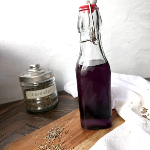 A bottle of lavender simple syrup on a wooden surface.