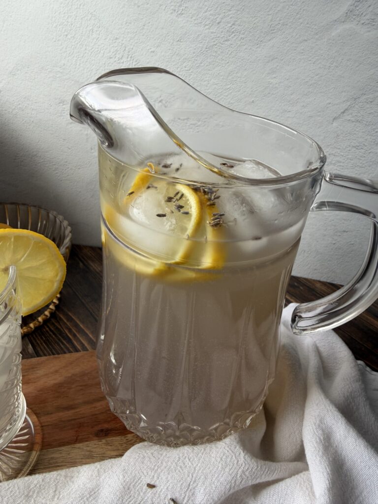 A crystal pitcher full of refreshing lavender kefir lemonade on a wooden surface ready to serve.