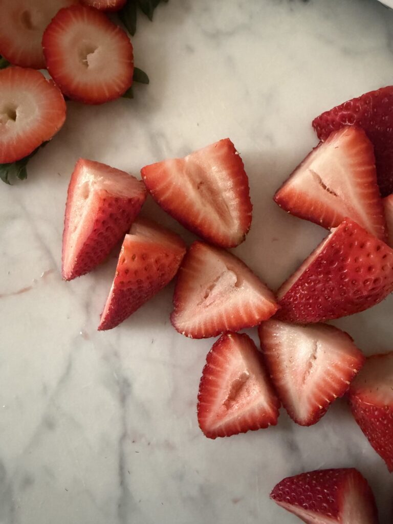 Fresh strawberries are sliced and scattered on a marble surface. 