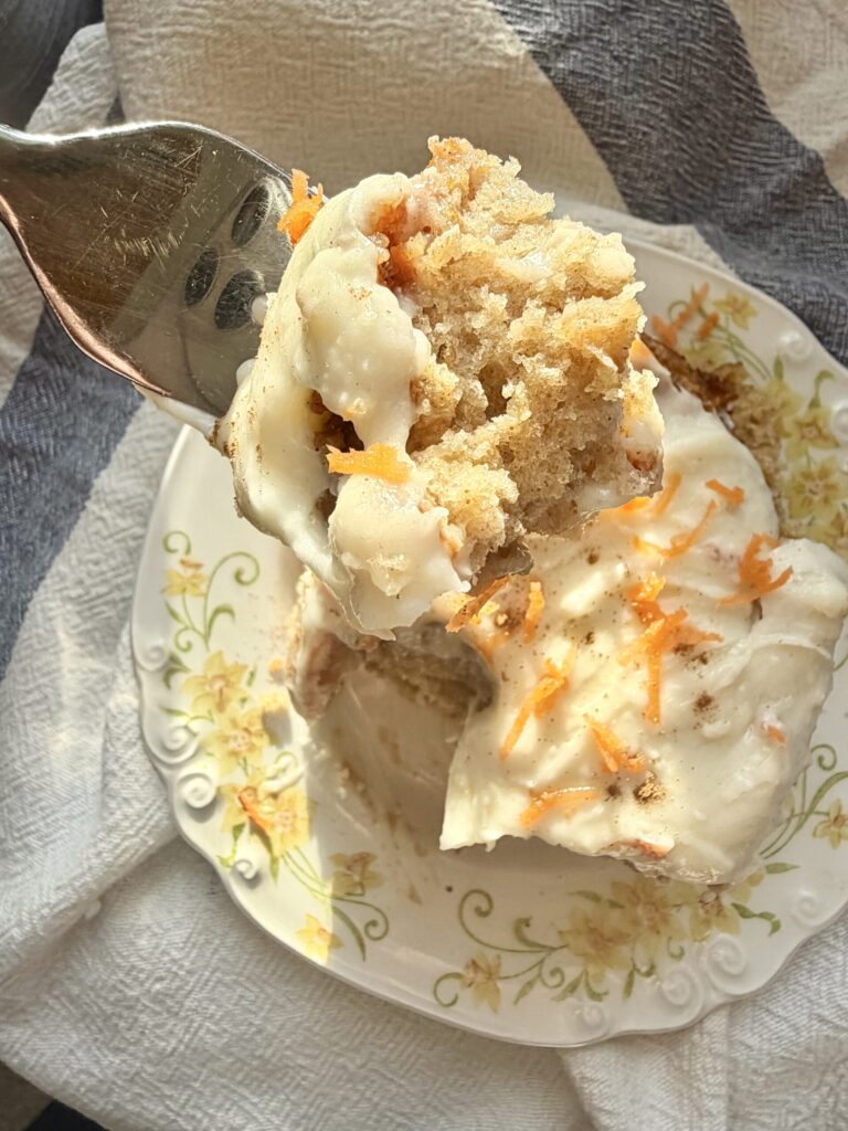 Carrot cake cinnamon roll on a white decorative plate topped with cream cheese frosting and shredded carrots