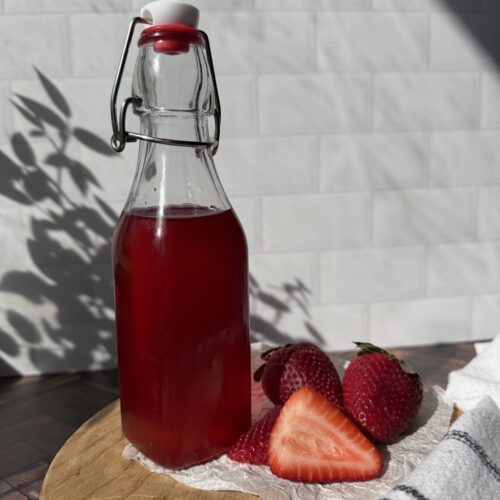 A bottle of strawberry simply syrup on a wooden surface with freshly cut strawberries.