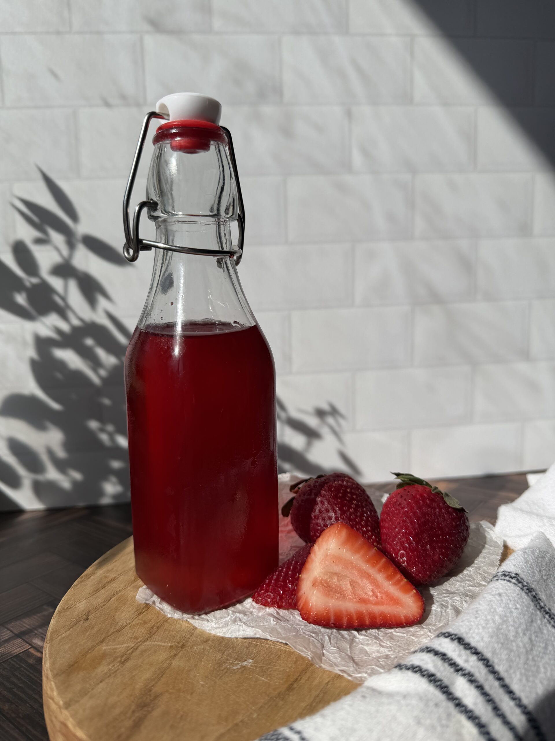 A bottle of strawberry simply syrup on a wooden surface with freshly cut strawberries.