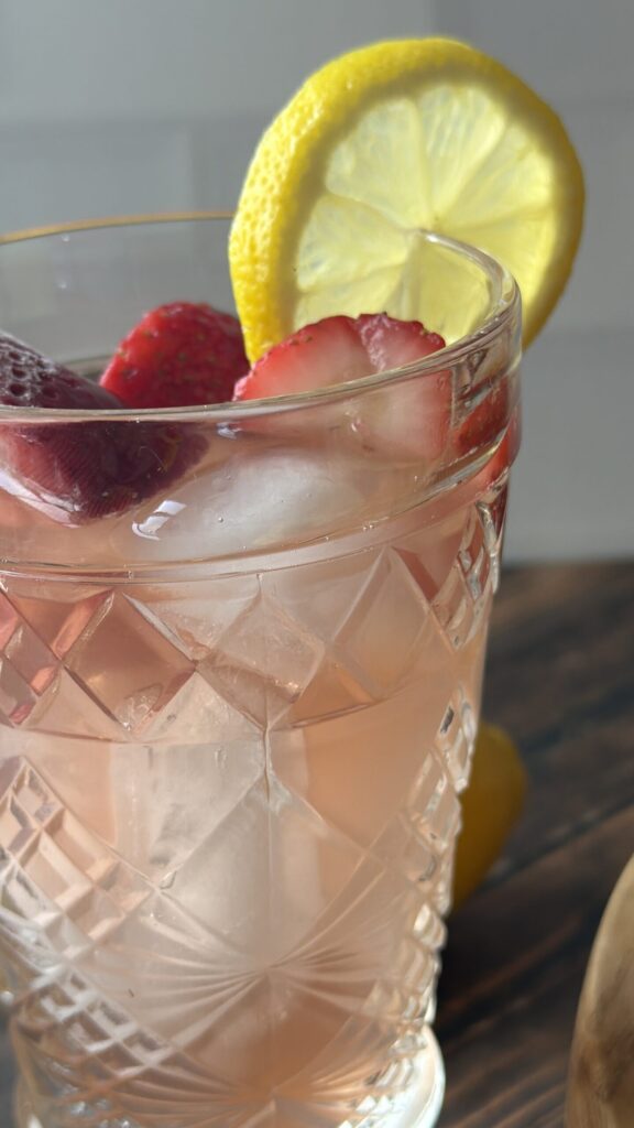 Closeup of a glass of fermented strawberry lemonade water kefir with fresh strawberries and lemon slices. 