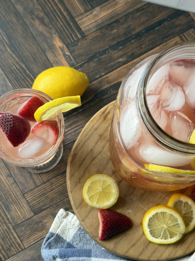 Probiotic rich strawberry lemonade water kefir on a wooden surface with sliced lemons and fresh strawberries. 