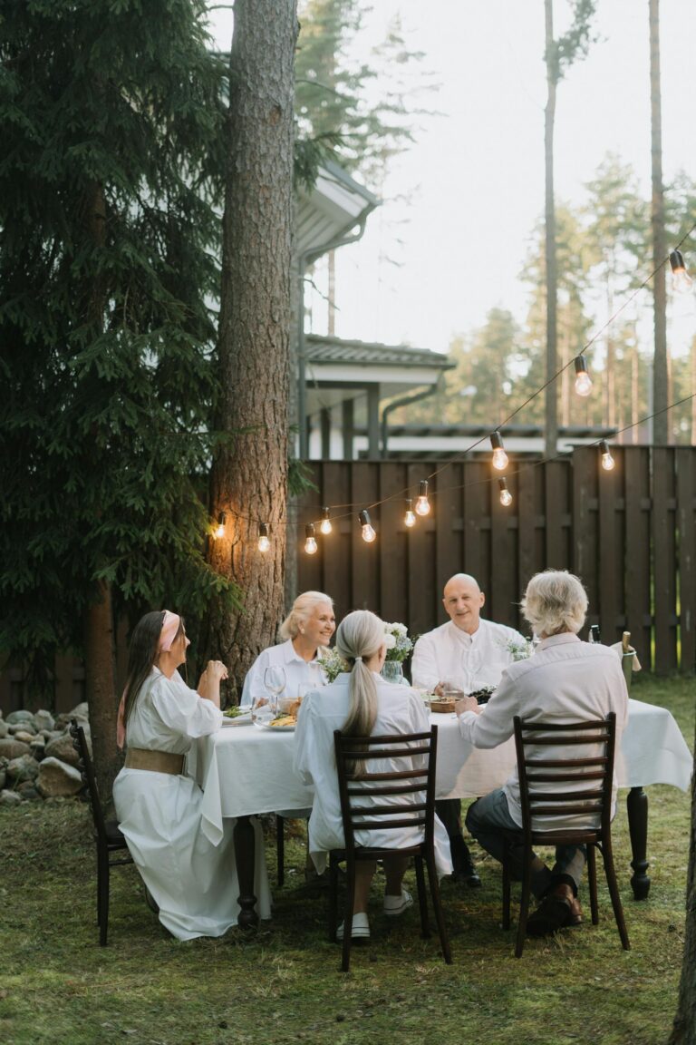 A group of senior adults enjoying a meal together in a lush outdoor setting.
