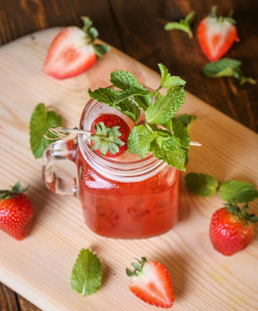 A refreshing strawberry and mint cocktail served in a glass jar on a wooden board, ideal for summer drinks.