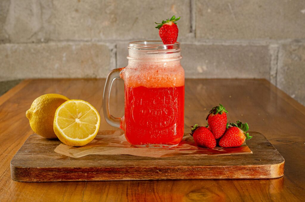 Refreshing strawberry lemonade in a mason jar with fresh fruits on wooden table.