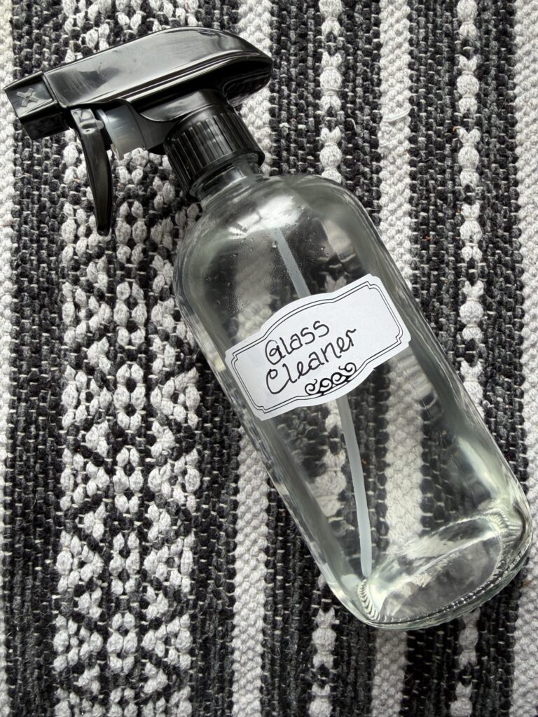 A glass bottle of homemade glass cleaner on a textured black and white surface.