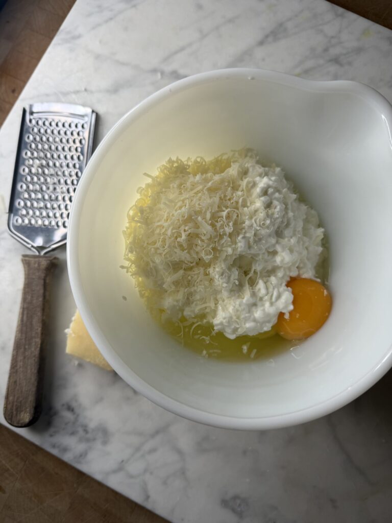 Cottage cheese, egg, and parmesan cheese in a white mixing bowl. 