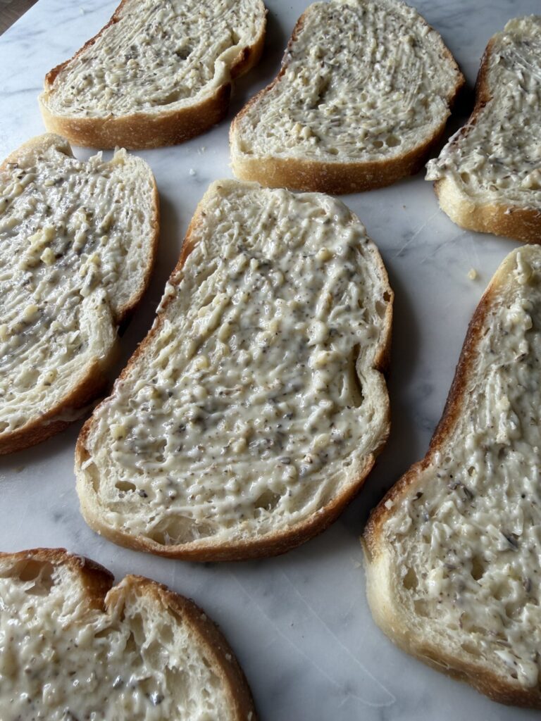 Sourdough bread slices with a garlic butter spread, ready to bake. 