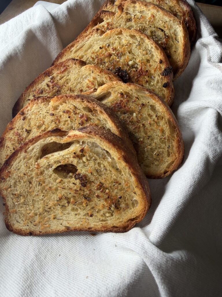 Crusty and buttery sourdough garlic bread slices in a basket lined with a tea towel.
