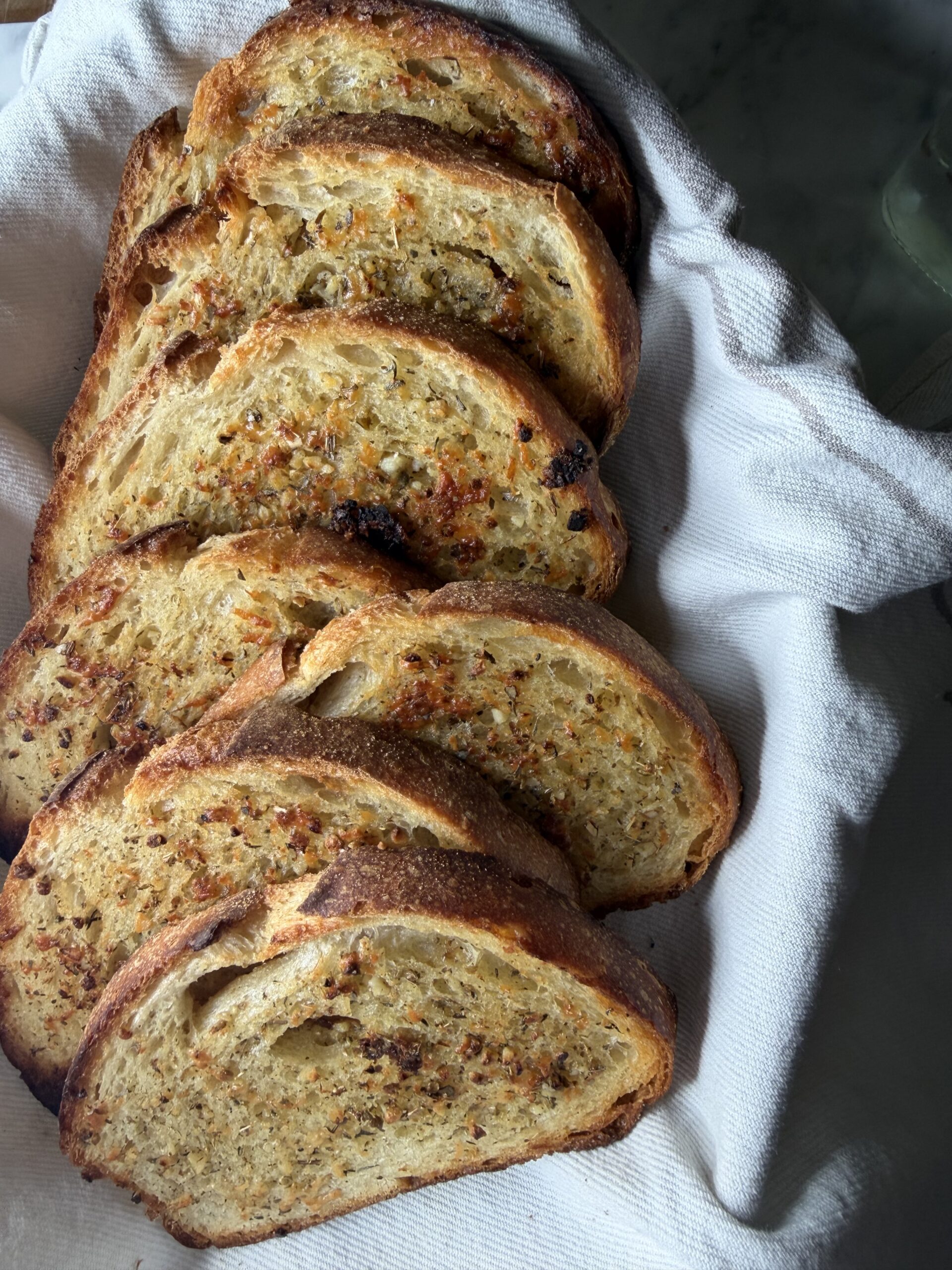 A golden stack of buttery sourdough garlic toast in a tea towel lined bread basket.