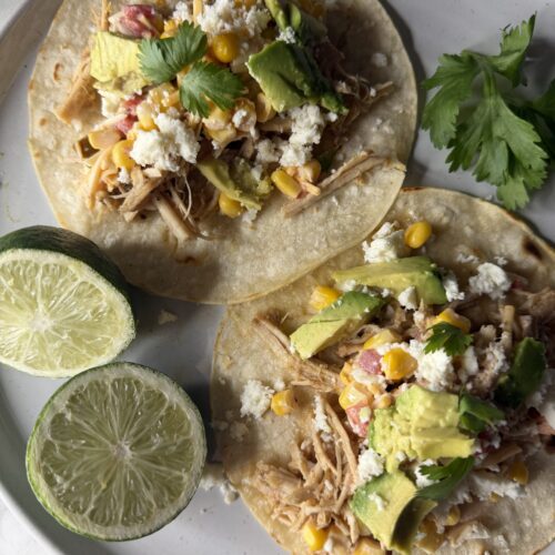 A delicious pork carnitas dinner on a plate with fresh lime wedges.
