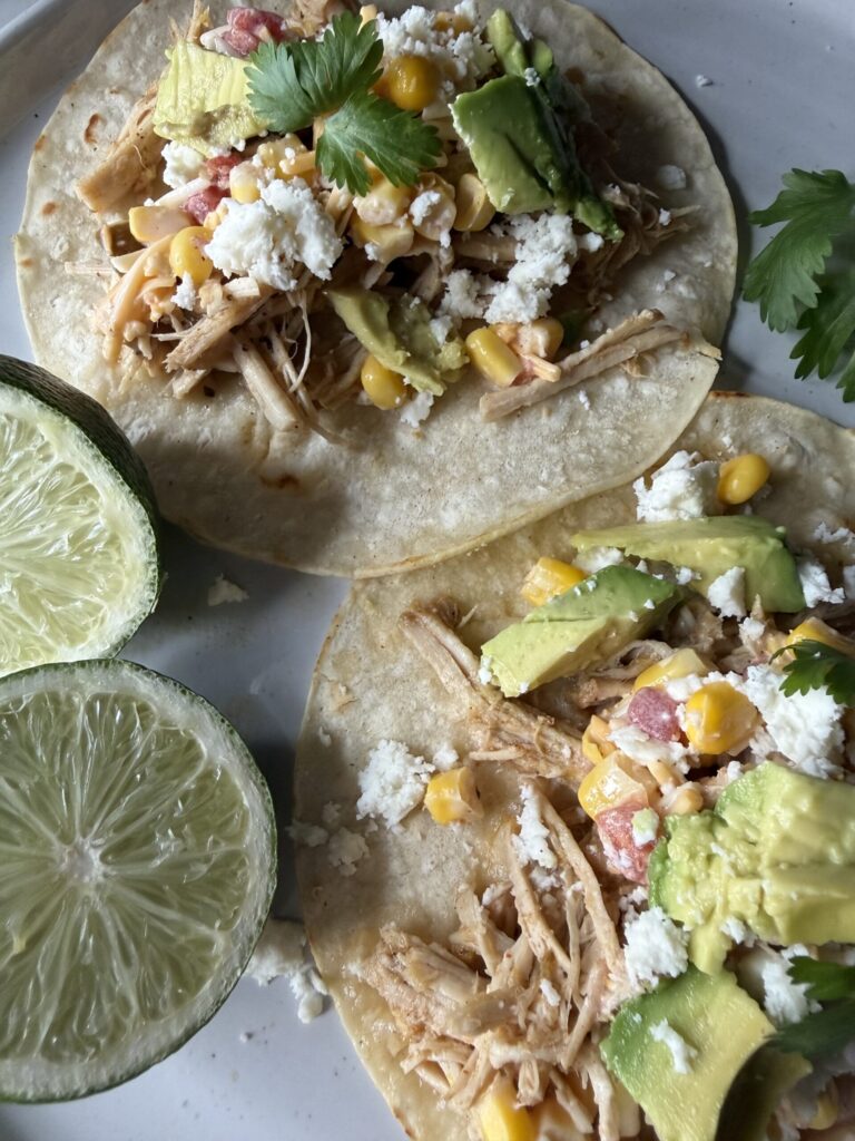 A closeup of homemade from scratch pork carnitas on a white plate with fresh limes. 