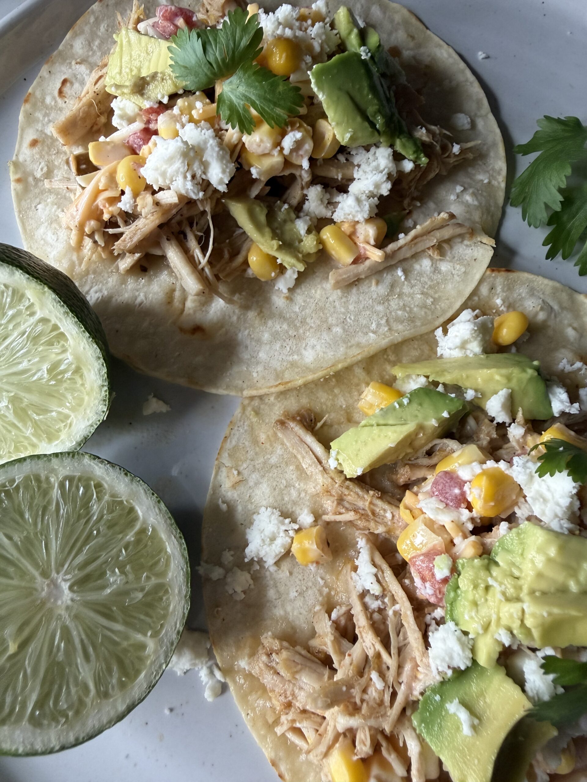 A closeup of homemade from scratch pork carnitas on a white plate with fresh limes.