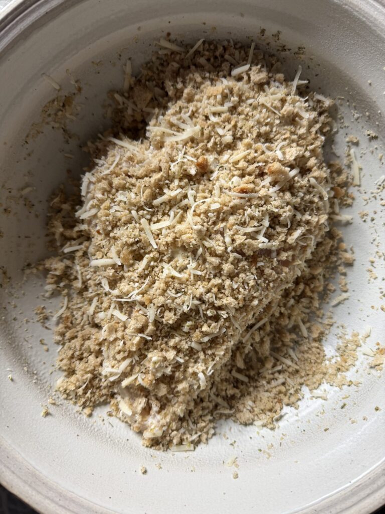 Chicken breast in a bowl covered with seasoned breadcrumbs. 