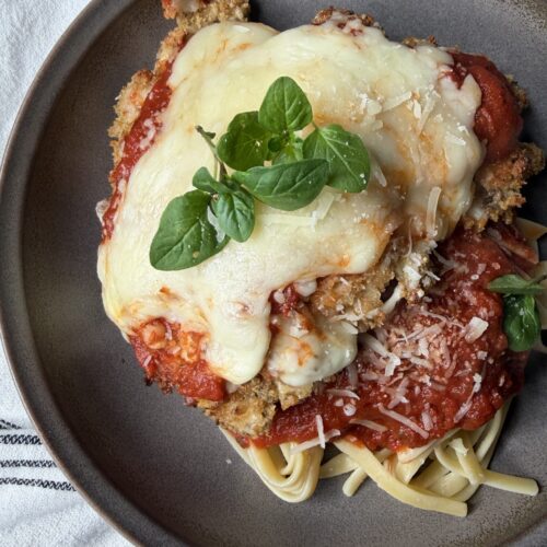 Homemade from scratch chicken parmesan with sourdough bread crumbs over pasta with marinara sauce.
