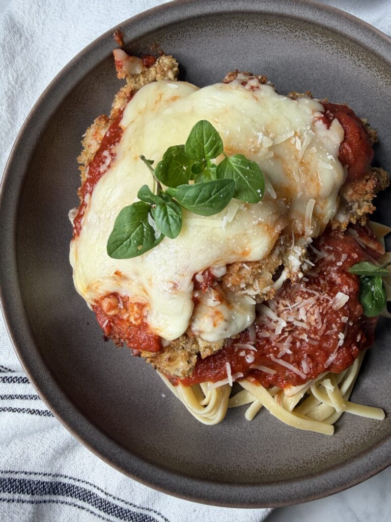 Homemade from scratch chicken parmesan with sourdough bread crumbs over pasta with marinara sauce.