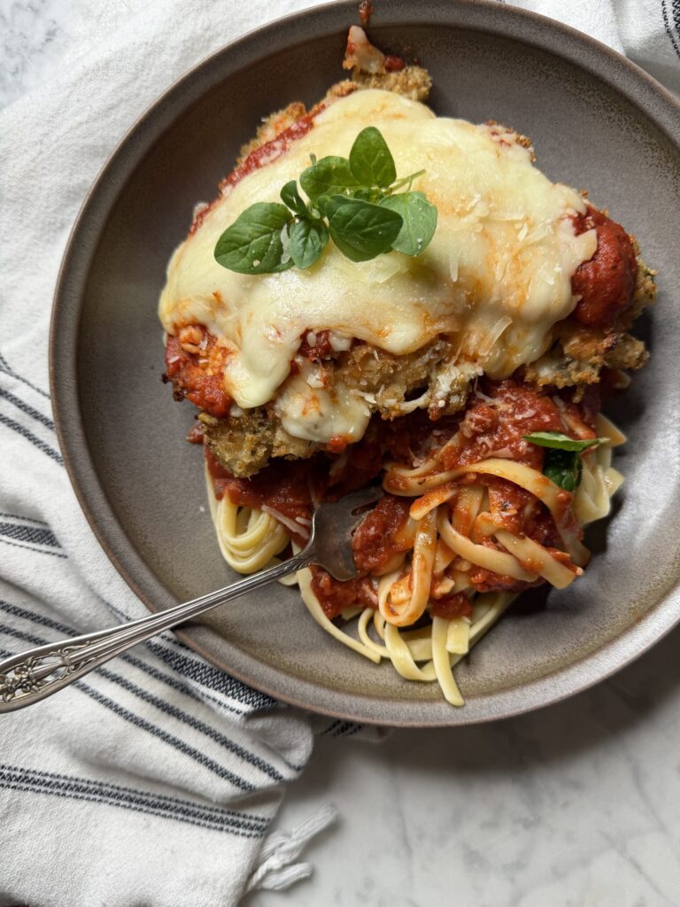 A forkful of sourdough noodles with marinara sauce topped with homemade chicken parmesan.  