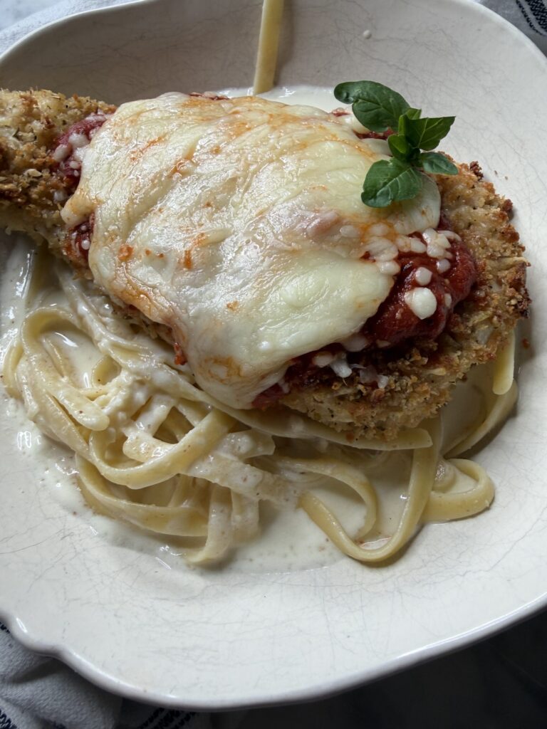 Homemade from scratch chicken parmesan over pasta with creamy alfredo sauce. 