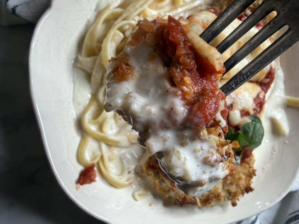Closeup of a bite of chicken parmesan with creamy alfredo pasta. 