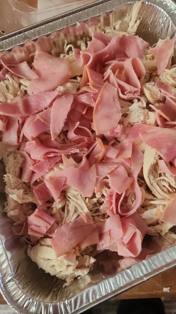 Chicken and ham are sprinkled and layered in a baking dish. 