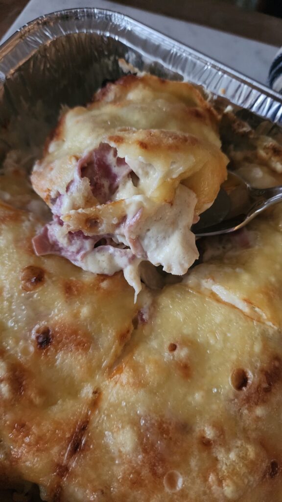 A slice of chicken cordon bleu casserole being scooped out of a metal pan ready to serve. 