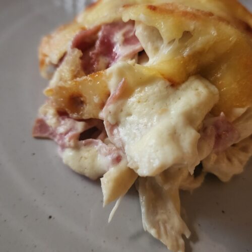 A slice of warm and creamy chicken cordon bleu casserole on a white plate ready to eat.