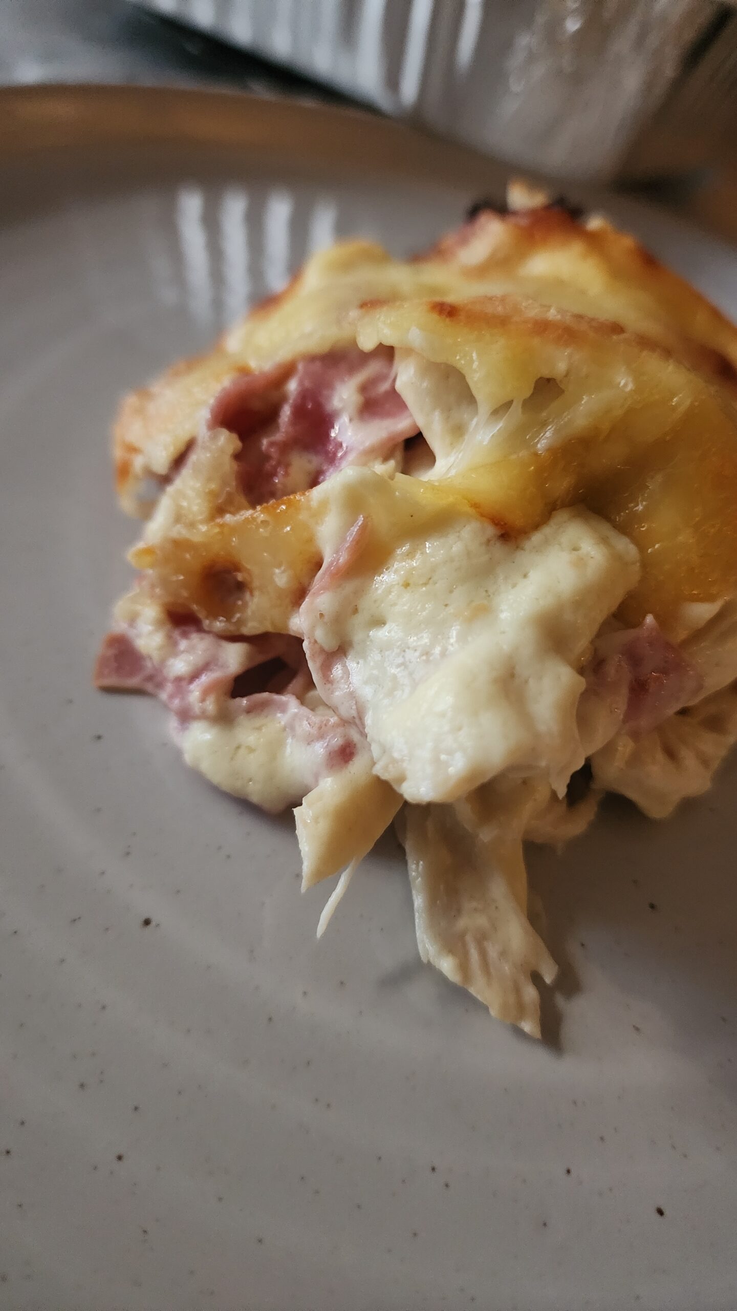 A slice of warm and creamy chicken cordon bleu casserole on a white plate ready to eat.