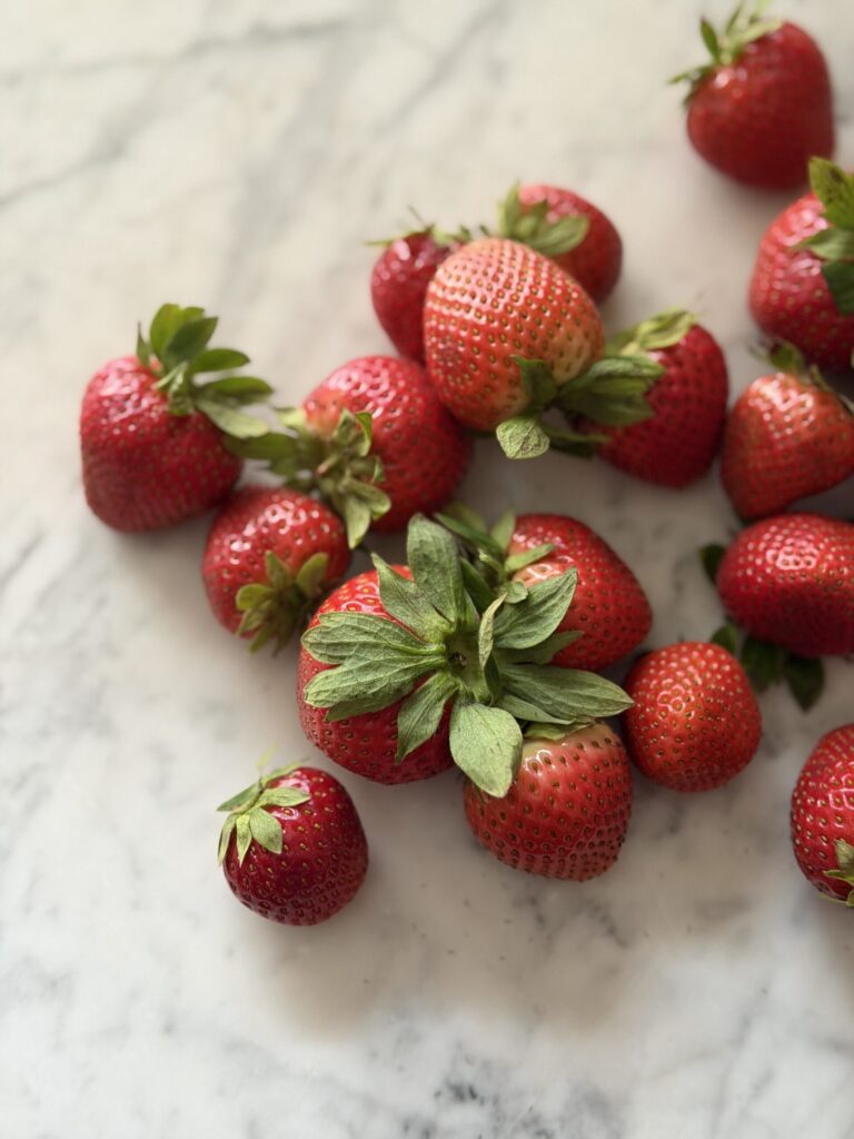 Strawberries are scattered on a marble surface ready to prepare to make a summery sourdough strawberry quick bread. 