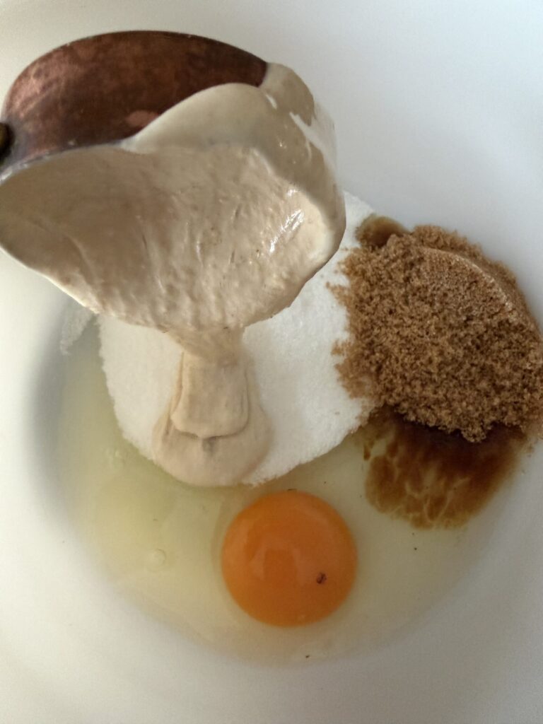 Sourdough starter, egg, and brown sugar are being added to a mixing bowl to make sourdough strawberry quick bread. 