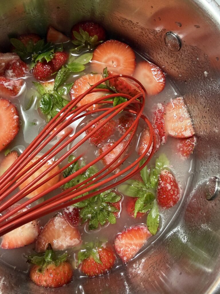 Strawberry tops and sugar are being whisked in a pan to make strawberry simple syrup. 